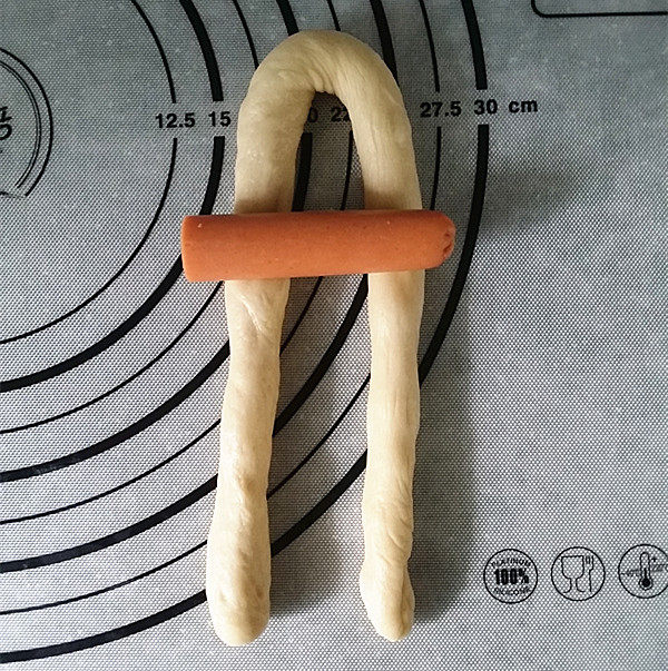 呆萌小兔子面包,取一根面团长条对折，在折弯1/3处，放上半根火腿肠