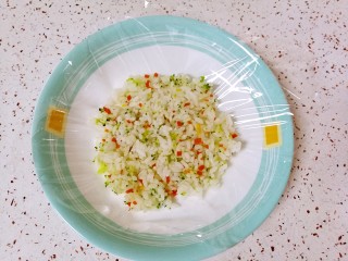 彩蔬饭团,取一张保鲜膜放在盘子里，放上拌好的米饭，用勺子背面压平。
