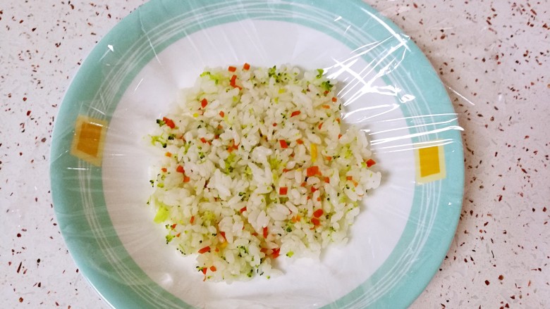 彩蔬饭团,取一张保鲜膜放在盘子里，放上拌好的米饭，用勺子背面压平。