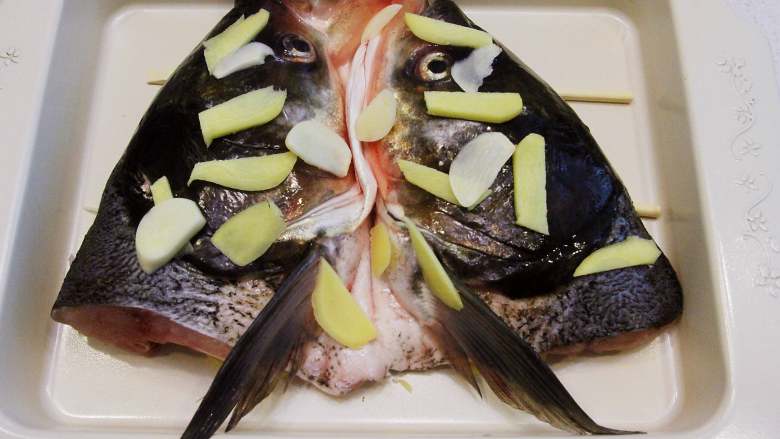 湘菜剁椒鱼头 新手家常菜,沥干水份的鱼头铺在上面，在鱼头上放上几片姜片，倒上5克料酒。