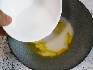 营养丰富的健康早餐之鸡蛋松饼,将牛奶倒入装载鸡蛋黄油的容器中，再把面粉和淀粉混合拌匀备用。
