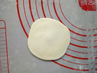 寿桃豆沙包,取一个小面团，摁扁后用擀面杖擀成边缘薄，中间厚的面皮。