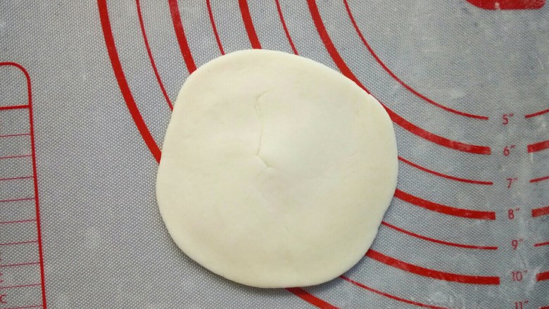 寿桃豆沙包,取一个小面团，摁扁后用擀面杖擀成边缘薄，中间厚的面皮。