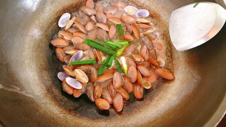 炒花蛤,炒均匀，先放入蒜苗，兑入适量开水。