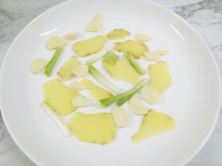 快手正餐 剁椒鱼头,把葱姜蒜洗净切好，摆放在盘子的底部。