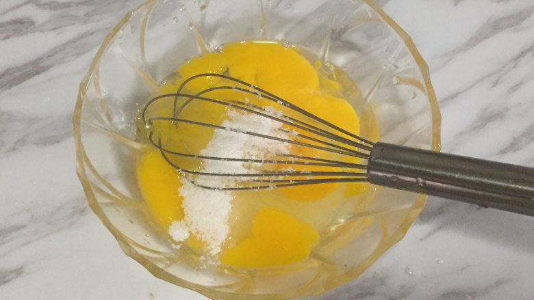 仿真栗子蛋糕,首先我们把三个鸡蛋打入碗中，一次性加入全部的白糖，用蛋抽搅拌均匀。