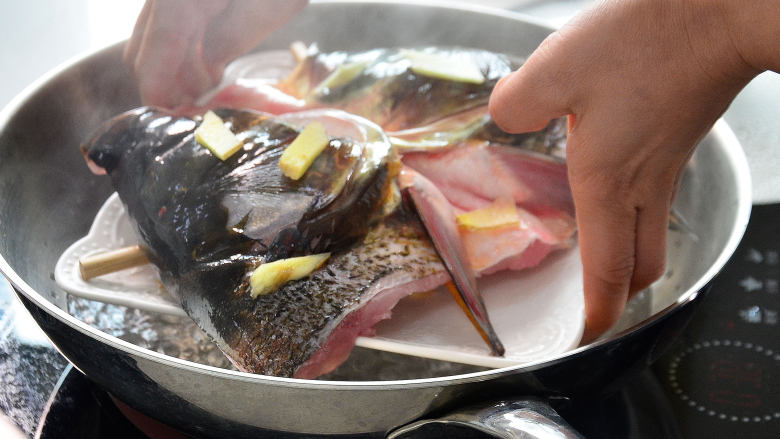 鲜美剁椒鱼头,锅加蒸架开火水烧开后把鱼头放入.大火蒸三分钟，取出来将碗里蒸出来的血水倒掉，去掉垫在底下的筷子，将拌好的辣酱料均匀的铺在鱼头上，入锅大火蒸6分钟