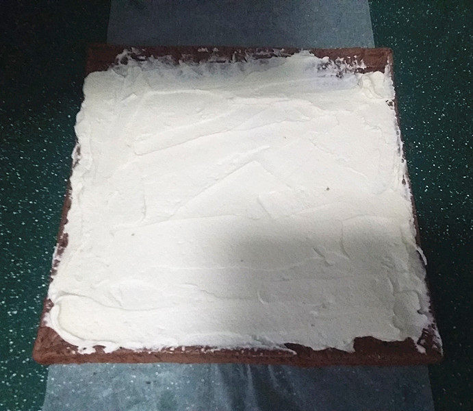 可可花奶油蛋糕卷,将蛋糕有花纹的那面铺在油纸上，然后将一半的奶油抹在蛋糕上、上面抹簿些、下端抹厚点