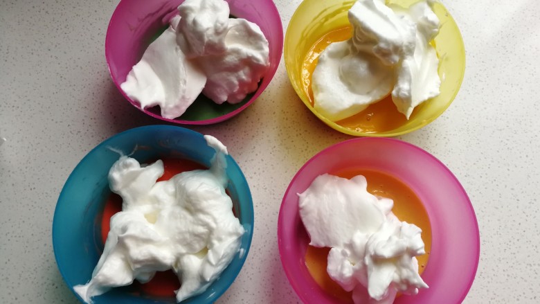 戚风棒棒糖蛋糕,接下来把打发好的蛋白霜，按先前一样的比例加入到四份蛋黄糊中，即原色蛋糊加约20克蛋白霜，彩色蛋糊加约30克蛋白霜。
