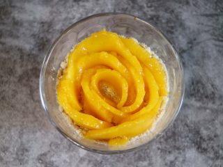 芒果木糠杯,最后在饼干屑的上面摆上芒花型,一片片的叠加摆出玫瑰花形状。