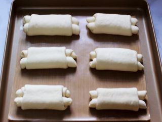日式牛奶面包卷（直接法）,把做好的面包翻过来，在烤盘上摆好后进行二发，现在的天气很热，不需要烤箱加热水一会就可以发好了