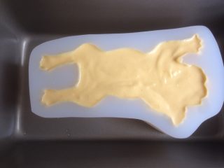 3D沙皮狗慕斯蛋糕,将芒果慕斯糊缓慢倒入沙皮狗模具里（模具需要提前几分钟从冷冻层取出来），利用小汤匙将慕斯糊划到不易流入的脚趾等部位，最后将模具在桌面上震动几下