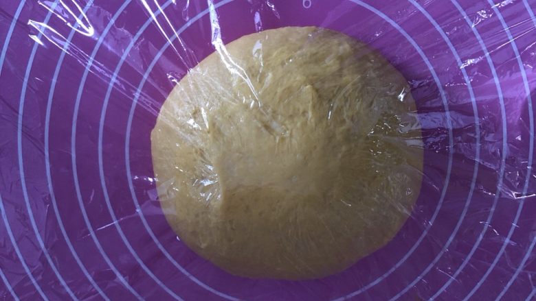 南瓜红豆吐司,经过三个揉面程序后，取出面团滚圆，置于案板上盖保鲜膜进行第一次发酵。