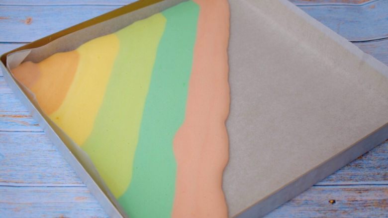 彩虹蛋糕卷,烤盘铺上油纸，先取一个色彩蛋糕糊剪掉底部，慢慢挤上去，一个颜色挤好接着一个颜色挤上