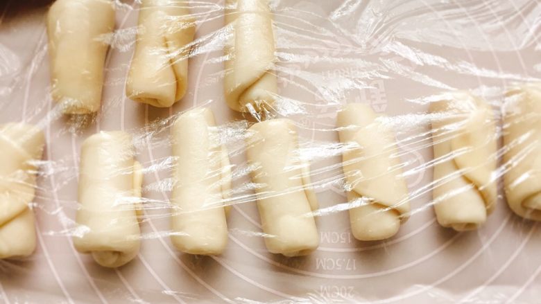 豆沙酥饼,翻面由下向上卷起，依次做完，覆盖保鲜膜松弛15分钟。