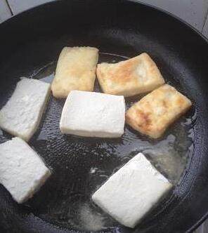 家常菜谱--葱烧豆腐,平底锅下食用油，油量覆盖锅底即可。淀粉盛在盘中，将豆腐均匀滚上一薄层淀粉，入锅小火煎黄。