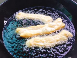 自制安心油条,等到油七成热时，将油条胚拉长之后慢慢放到锅里进行炸制。