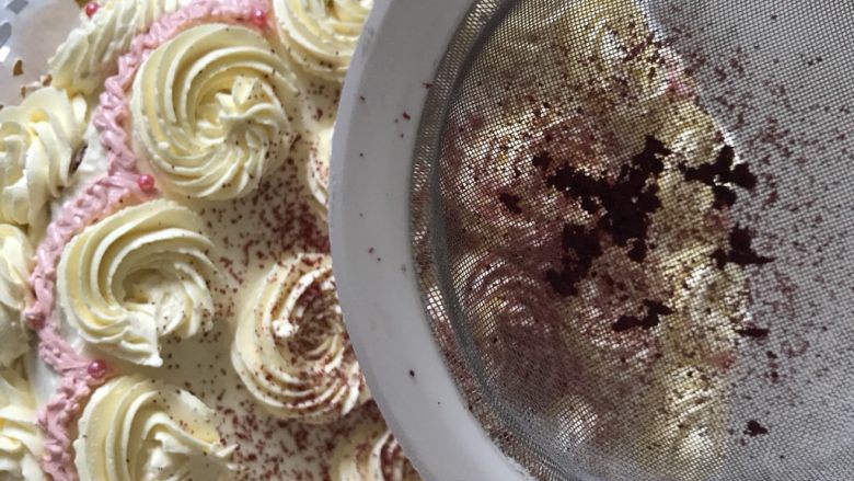 10寸红丝绒蛋糕,之后就可以裱花啦，这种奶油霜一般不容易融化，适合用于裱花，从底层开始裱花，一直到最上面，然后把之前看蛋糕时蛋糕坯子上掉下来的蛋糕碎削放进过滤网用手碾压筛出红丝绒粉。