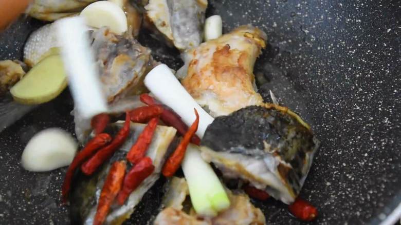 鲜香不腻，味道实在太好吃的红烧三文鱼头煲,热锅冷油，放入鱼头，煎至微焦。
再倒入葱、姜、蒜、干辣椒，炒匀。