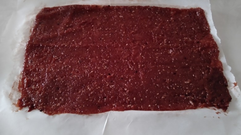 蜜汁猪肉脯,铺在油纸上，上面也铺一张油纸，慢慢的擀成0.3厘米厚，借助刮板整形后，拿掉上面的油纸。