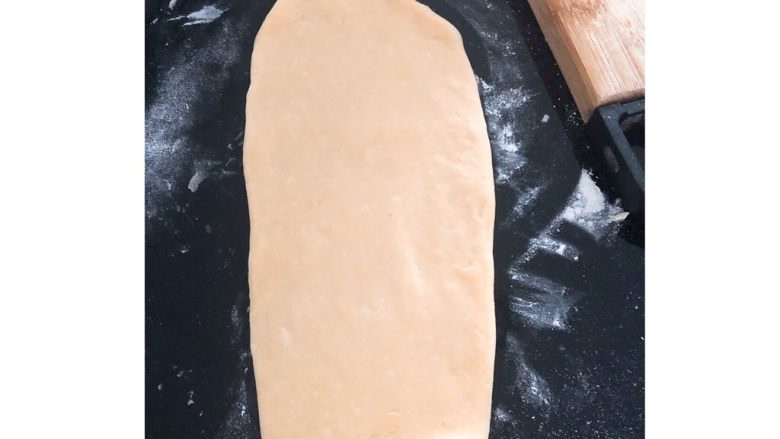 葱香火腿腊肠肉松面包,将面团揉成6个小面团，用擀面杖擀成如图示的长面饼。（擀面饼时面板需撒一层薄面粉，否则面饼会粘在面板不易取出）
