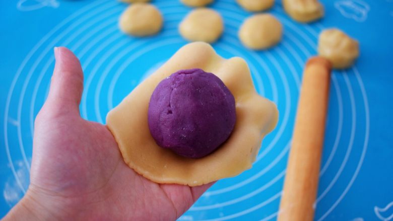 紫薯蛋黄月饼,取一份饼皮，放在掌心按压成圆饼形，再放入紫薯蛋黄馅