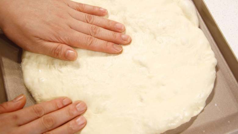 佛卡夏|有料又快手的面包,方形烤盘中扫适量橄榄油，将醒发好的面团适量拍扁后放入烤盘中，用十个手指尖戳捣变平。