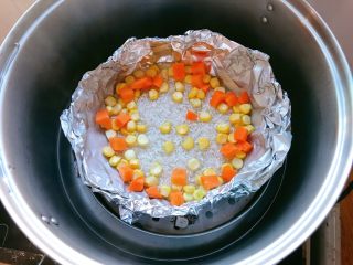 香辣肥牛蒸饭,锡纸做成碗形，放入大米，加入适量水，边上放入玉米粒和胡萝卜丁。盖上盖子蒸。