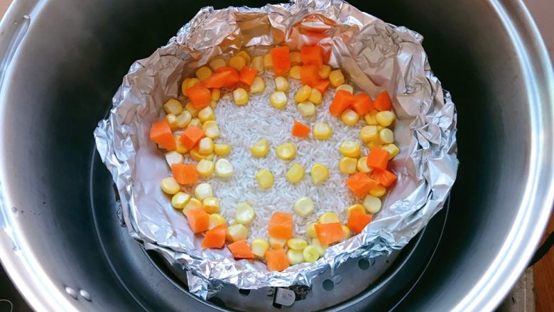 香辣肥牛蒸饭,锡纸做成碗形，放入大米，加入适量水，边上放入玉米粒和胡萝卜丁。盖上盖子蒸。
