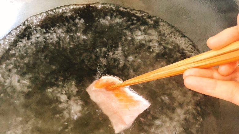 白灼沙拉三文鱼-西餐、年夜饭,锅里烧开水，用筷子夹着三文鱼片逐片放入水中。