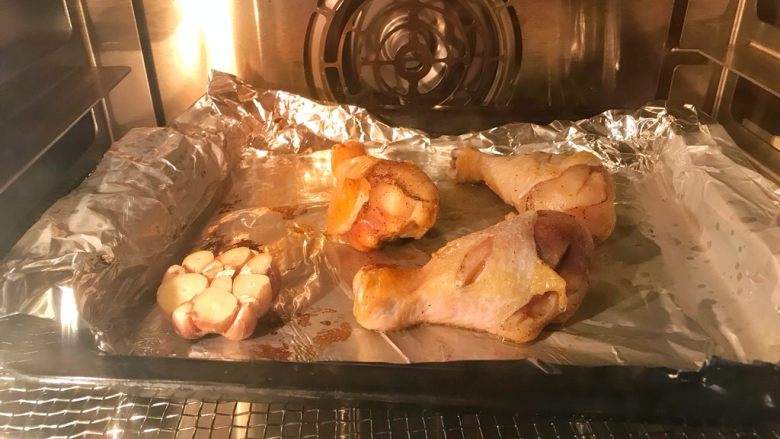 脆皮烤鸡腿,烤箱预热190℃，烤盘垫锡纸，刷上油防粘。放上鸡腿，并在鸡皮上刷油，先放入鸡腿和蒜190℃烤15分钟。