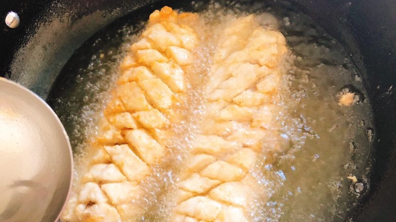 酸甜脆皮菊花鱼-年夜饭,锅里倒油烧热，放入鱼肉油炸，并用勺子将油不断从上往下浇，使得鱼花开出。