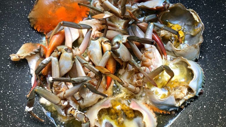 肉蟹煲,锅里放入适量油，把沾好淀粉的蟹肉，切口朝下放到油里煎制，蟹壳也一起放入