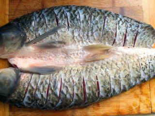 香辣烤鱼,鱼洗干净放到案板上，用刀在鱼身上划斜刀（间隔1cm划一刀），这样方便入味