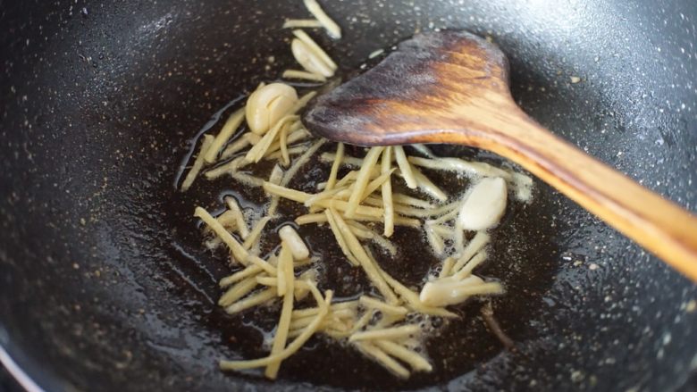 鳝鱼炒菜脯,锅里热油后放入姜丝和蒜瓣煸出香味