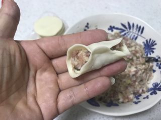 家常酸汤莲菜大肉水饺,拿一个饺子皮包入饺子馅，先捏中间。