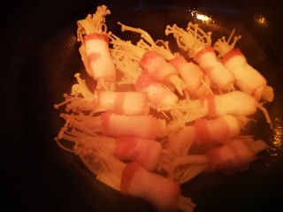 金针菇培根卷,锅中放入少许玉米油，油热后放入培根卷小火煎