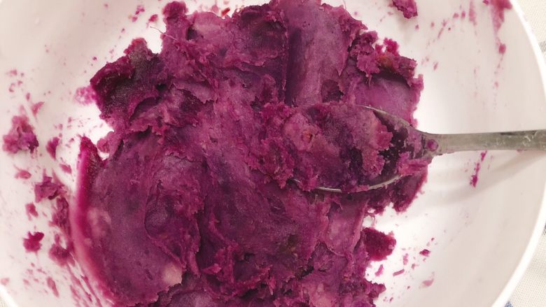全脂奶香紫薯馒头,拿一根煮好的紫薯，剥去皮，将紫薯放到一个碗里，用勺子搅烂。