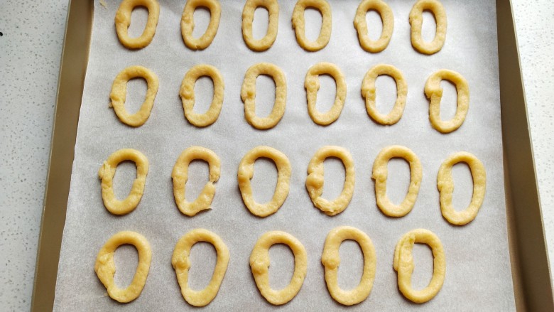 罗马盾牌饼干,接下来把裱花袋中的面糊，在烤盘中的油纸上挤成椭圆形的小圈圈。