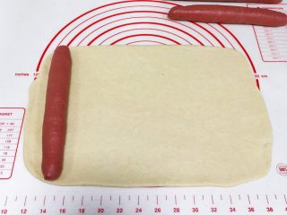 红曲双色椰浆面包,把白色的面团擀成长约30厘米，宽约18厘米的长方形片状，把一根红色长面团放在面片的左边。