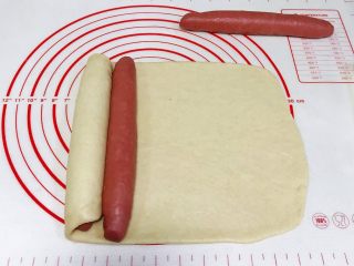 红曲双色椰浆面包,白色面片往右边卷起红色长面团，盖住后再放上第二个红色面团。
