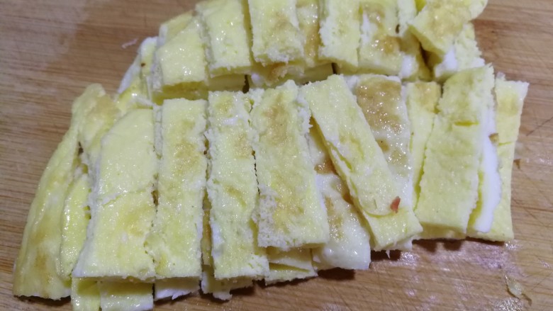 牛肉蒜薹炒蛋条,煎熟的蛋饼放在案板上，用刀切成小条，如图↑