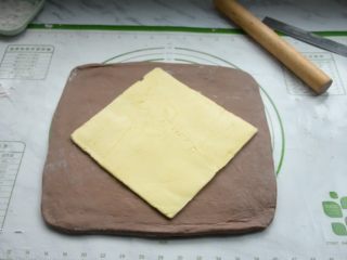 脏脏包,将松弛好的面团取出，在硅胶垫上撒些面粉放粘连，再把面团擀成比黄油片稍大的面片，把黄油片放在中央。