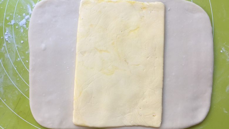 双色牛角酥,冰箱取出冷冻的黄油片，用刀裁开保鲜袋，将黄油片放在面片中间 