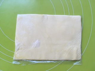 双色牛角酥,将软化的黄油用手一点点捏入保鲜袋的两个角，之后将保鲜袋对折，用擀面杖擀平正，擀成薄片，之后入冰箱冷冻 
