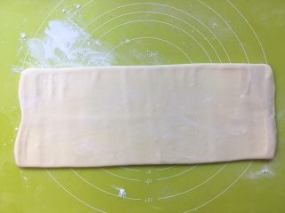 双色牛角酥,撒点干粉，将面片对折处朝下放，用擀面杖一点点从中间向前向后推擀面片，将面片擀长，长度大约为40厘米