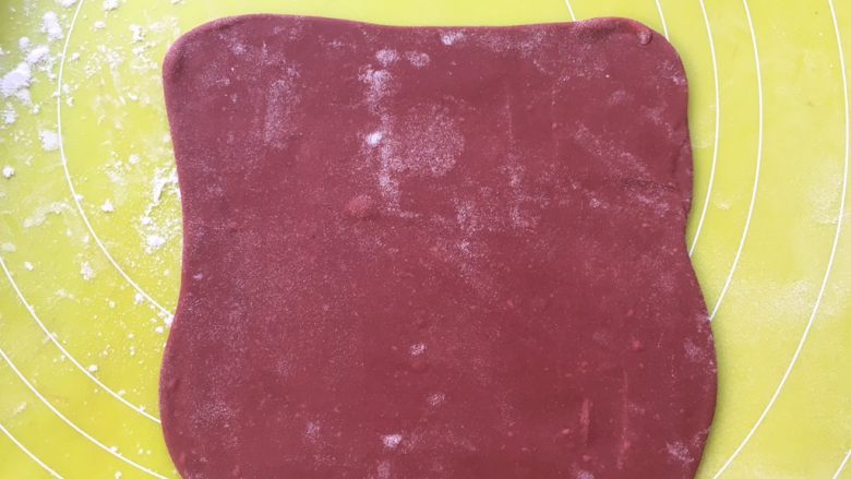 双色牛角酥,将红色面团擀成方形，不用太大，之后包裹油纸装入保鲜袋入冰箱冷冻