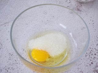 红丝绒心形玛德琳蛋糕,鸡蛋打入盆中，加入白糖，用手动打蛋器搅拌至白糖融化