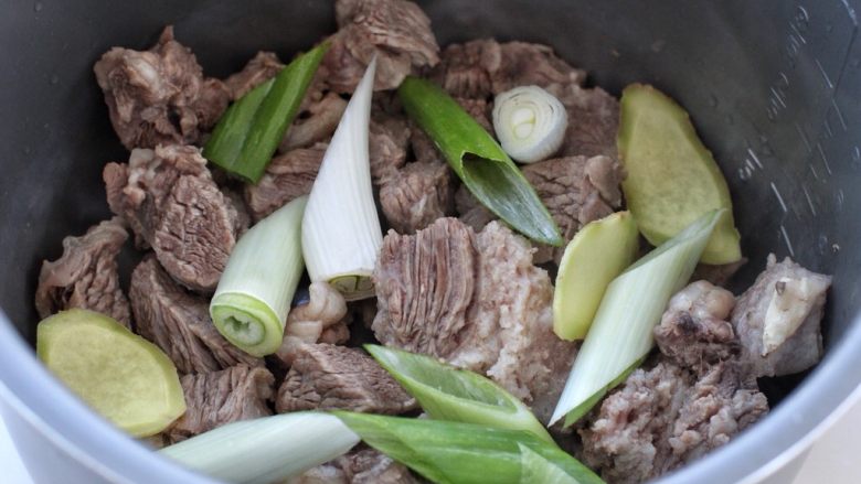 清炖牛肉萝卜汤,将牛肉块放入高压锅内胆中，接着放入葱段和姜片