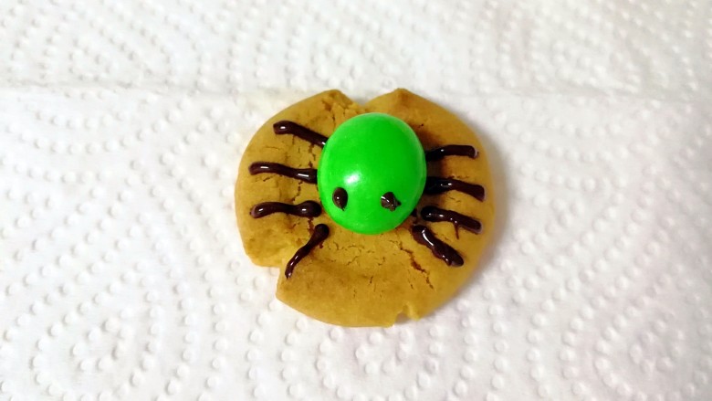 万圣节蜘蛛饼干,继续用裱花袋画出蜘蛛的眼睛和腿，一个萌萌的蜘蛛饼干完成了。